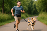Man running with a dog on a lead and a waist bag in a park area.